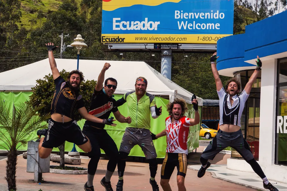 Five riders leaping in the air in front of the Welcome to Ecuador billboard.