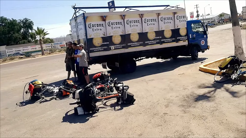 A Corona beer truck parked by the road, with loaded touring bikes lying on the ground beside it.