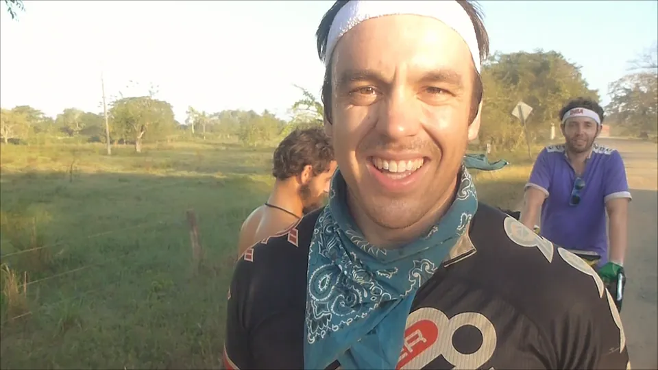 A grinning rider in a bandana, with another rider behind him on a Colombian road.