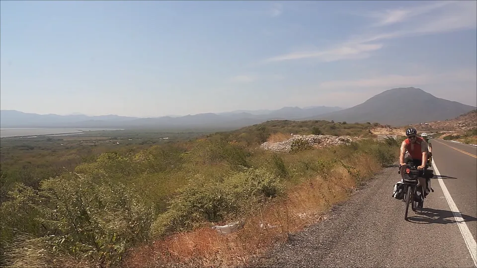 A lone rider on an empty road across the Isthmus of Tehuantepec, with a mountain on the horizon.