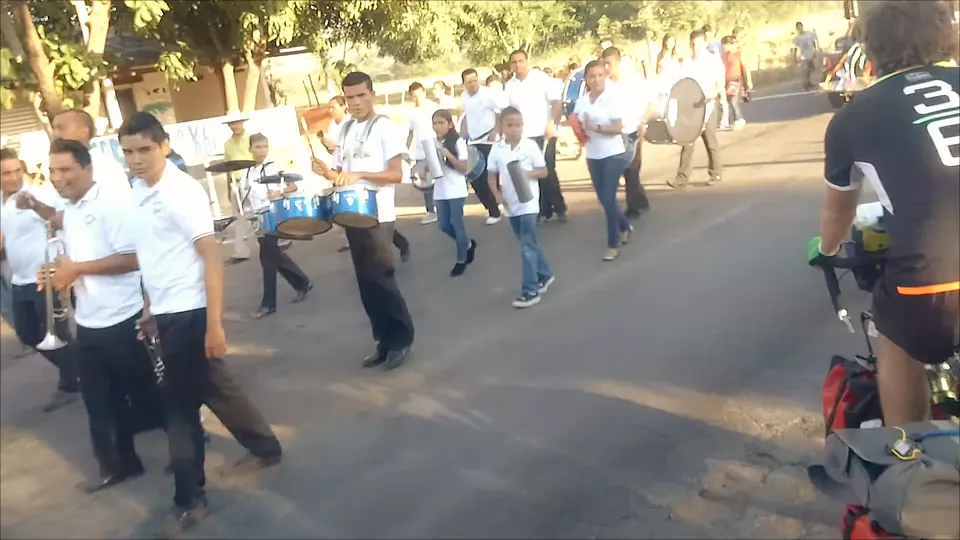 A marching band in white shirts parading down the road at the border.