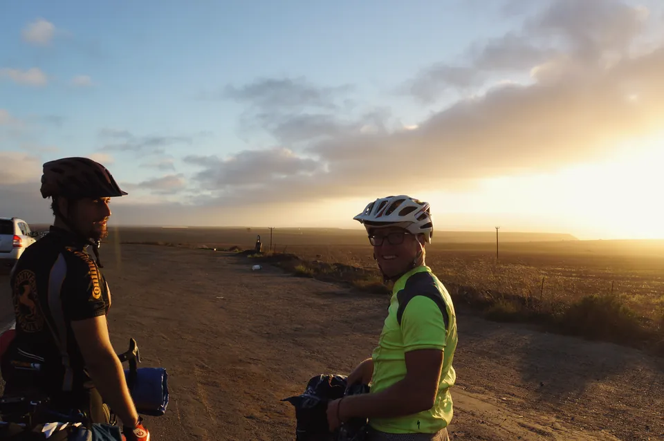 Two riders grinning into the low evening sun beside farmland in Baja.